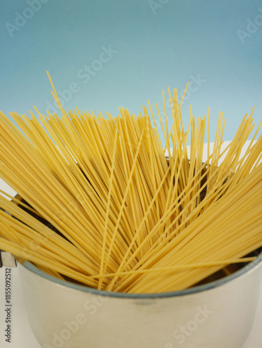 Wallpaper Mural Tall vertical image of uncooked spaghetti rising from a shiny metal saucepan on blue and white background, modern food photo of dry pasta cooking ingredients Torontodigital.ca