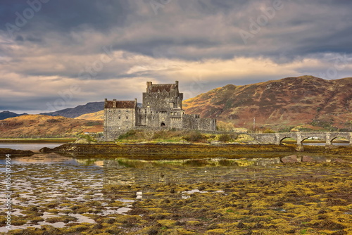 Sunny moment on a cloudy day lighting Eilean Donan tidal island-castle at low tide, linked to the mainland by a stone footbridge. Dornie-Scotland-187