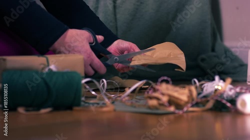Hands cutting Christmas gift wrapping paper with ribbon and string green background