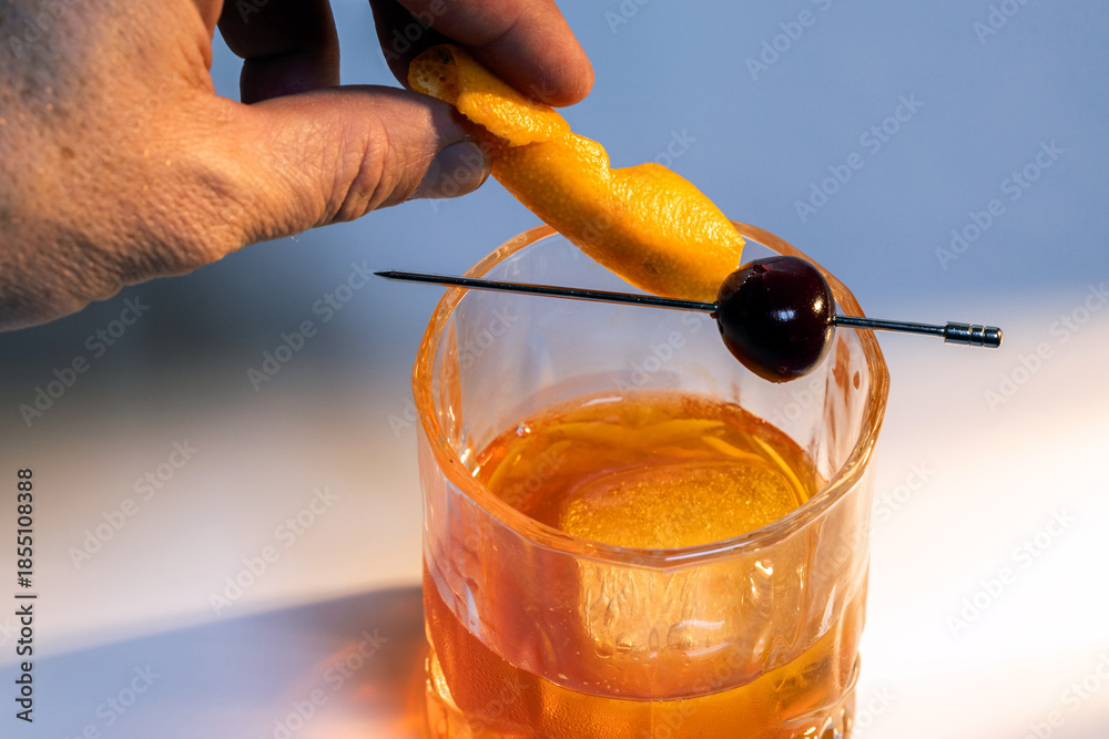 custom made wallpaper toronto digitalClose up of a hand placing an orange slice in a manhattan cocktail served with one large ice cube on a reflective white surface.