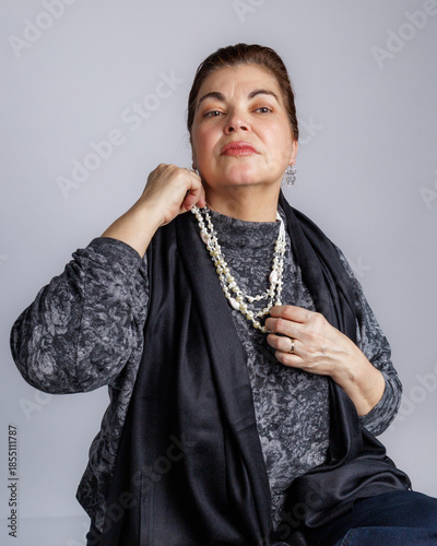 Woman adjusting a layered pearl necklace while posing confidently against a neutral background.