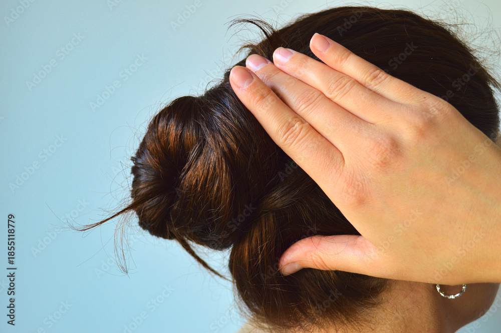 Fototapeta premium Close-Up of a Woman Smoothing Her Hair Bun with Her Hand