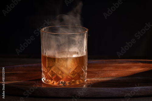 Smoked whiskey cocktail served on the rocks with dramatic lighting served on a wooden surface.