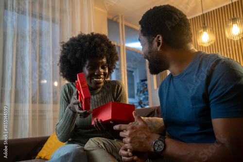 Obraz na płótnie Black man giving gift to woman, she is excited and happy in living room