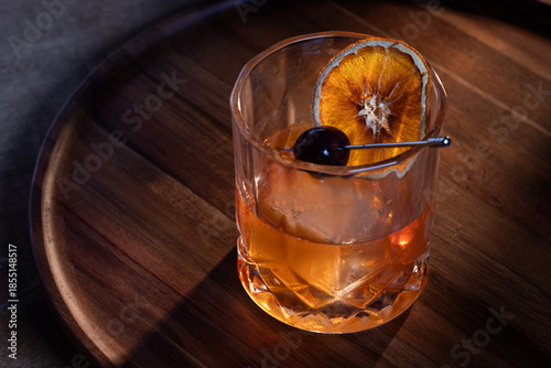 whiskey cocktail served on the rocks garnished with a dehydrated orange slice with dramatic lighting served on a wooden surface.