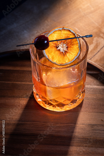 Beautiful garnish of a dehydrated orange slice and a dark cherry on a whiskey cocktail served on the rocks.