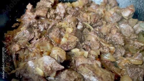 Close up of beef liver with onions frying in a pan with steam, delicious rustic cooking process