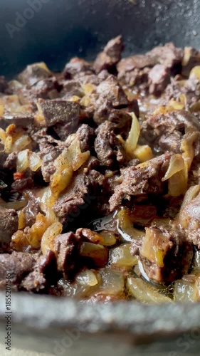 Close up of beef liver with onions frying in a pan with steam, delicious rustic cooking process