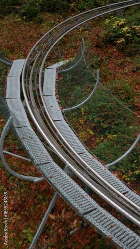 A sports slide, an amusement park, and a descent in the forest in the mountains. Dense trees with orange autumn leaves.