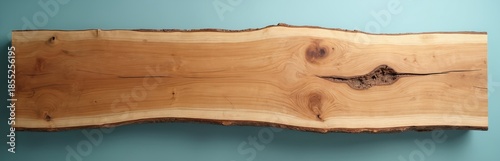 Natural live edge slab of light brown wood with visible grain patterns and bark. Clean light blue background accentuates organic texture. Ready for use as tabletop or furniture element.