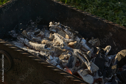 Smoldering logs and bright flames in a metal barbecue grill. Detailed close-up of fire, heat, and smoke outdoors. Flaming logs with heat and smoke rising from an open grill.