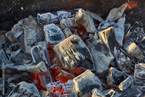 Smoldering logs and bright flames in a metal barbecue grill. Detailed close-up of fire, heat, and smoke outdoors. Flaming logs with heat and smoke rising from an open grill.
