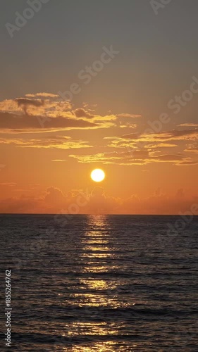 Beautiful orange sun slowly sinking below the horizon over the rippling ocean. Golden sunlight reflects on the tranquil water surface