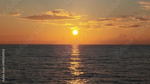 Golden sunrise over the tranquil ocean, casting a stunning play of light on the water's surface. The seascape is peaceful with wispy clouds scattered across the sky