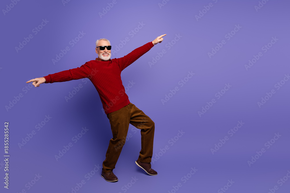 Fototapeta premium Joyful mature gentleman in red sweater dances away purple background for fashion style lifestyle advertising promotional imagery with humor and energy