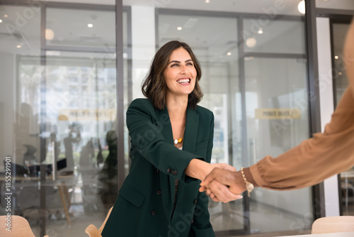 Happy young Hispanic businesswoman shaking hands with female partner, coworker, advisor, consultant. Latin candidate getting job after successful interview, giving handshake to recruiter