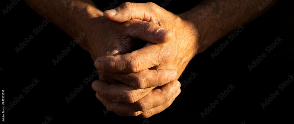 Fototapeta premium Close up of elderly man's hands clasped together in low key lighting