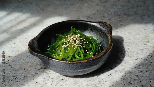 Close-up of a sushi bowl topped with seaweed and garnished with white rice grains. The dish is placed on a white marble table.