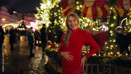 Graceful pregnant woman in stunning red gown amidst festive market ambiance with soft lighting slow motion