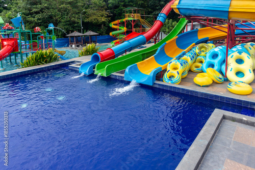 Colorful waterpark slides in outdoor swimming pool, empty aquapark with blue water, happy fun bright vibrant holiday vacation