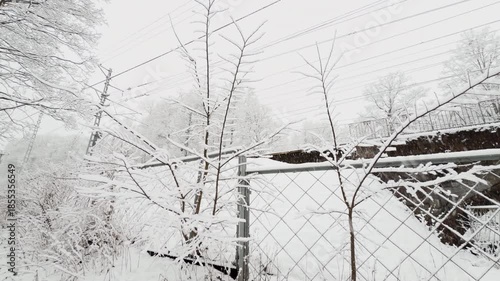 Russia, St.Petersburg, it is snowing heavily in the park, An electric train passes over an archway, large flakes of snow are slowly falling on tree branches