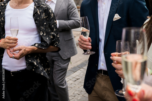 Slika na platnu Well-dressed guests holding champagne glasses at an outdoor celebration, stylish social gathering on a cobblestone street capturing elegance, fashion, and festive atmosphere