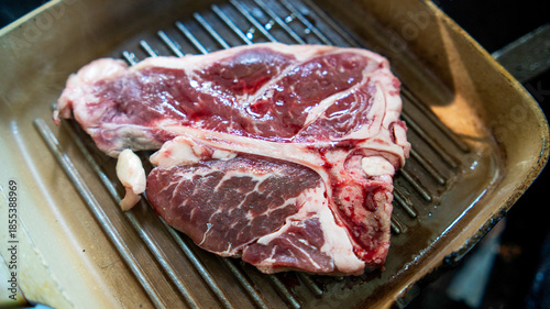 Raw beef steak placed on hot grill pan ready for cooking, showing marbled texture and fresh cut of meat, Concept of culinary preparation gourmet cooking.