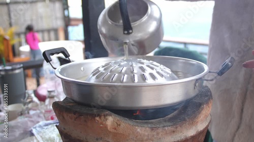 4K Traditional Asian barbecue grill pan placed on a charcoal stove with hot water being poured to prepare for cooking, Concept of local cuisine comfort food street food culture.