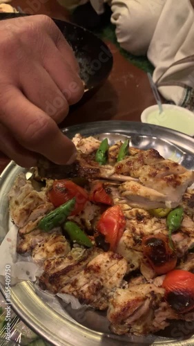 A top-down, close-up shot of traditional Pakistani Chicken Malai Boti served on a silver platter. The dish features succulent, charred pieces of boneless chicken marinated in a creamy white sauce.