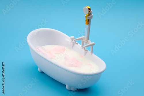 Milk Bath Spa Concept with Rose Petals Floating in Mini Bathtub on Blue Background