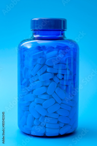 Medicine, pharmaceutical industry and headache medication concept with white pills in transparent plastic bottle isolated on blue background