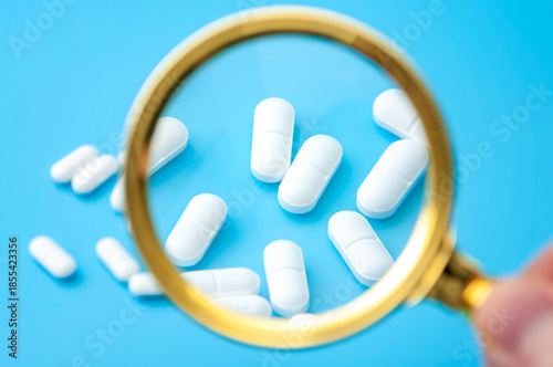 Laboratory investigation, medication inspection and pharmaceutical industry review with scientist using magnifying glass to zoom in and examine many prescription drugs isolated on blue background
