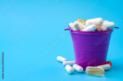 Excessive supplementation, wellness and wellbeing concept with many mixed vitamins and supplements in a metal bucket isolated on blue background with copy space