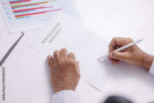 Person is signing non disclosure agreement at desk, with colorful charts visible in background, indicating business setting