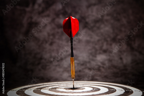 Dart arrow hitting the center of dartboard with red dart arrow