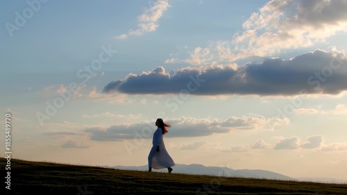 Serene Woman Walking at Sunset in a Flowing White Dress on a Hill
