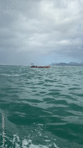 Vertical footage of a traditional wooden boat navigating the turquoise waters of remote Sulawesi, Indonesia. Essential maritime transportation in an isolated archipelago under a cloudy sky.