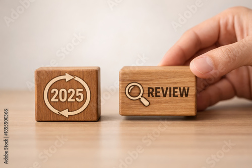 Hand arranging wooden block with year 2025 and magnifying glass icon for annual review concept showing business evaluation