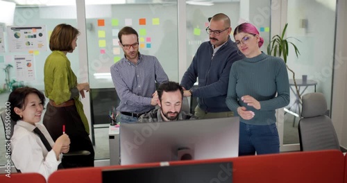 Team members discuss project ideas and collaborate in an office setting with a focus on a man at a computer and group engagement