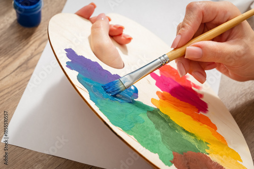 A person is painting a palette with a brush. The palette is full of different colors. The brush is being used to paint the palette