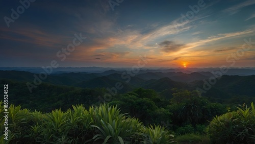 Panoramic nature view of a golden sunrise and sunset over misty mountain peaks where clouds float above a forest valley at dawn and dusk