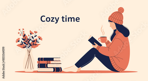 Young woman enjoying a cozy time in autumn or winter, reading a book and sipping a hot drink while sitting on the floor.