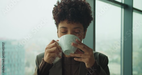Person features warm smile while holding coffee near city window