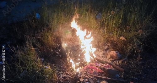 Nighttime close up: bright flames consuming plastic and weeds.