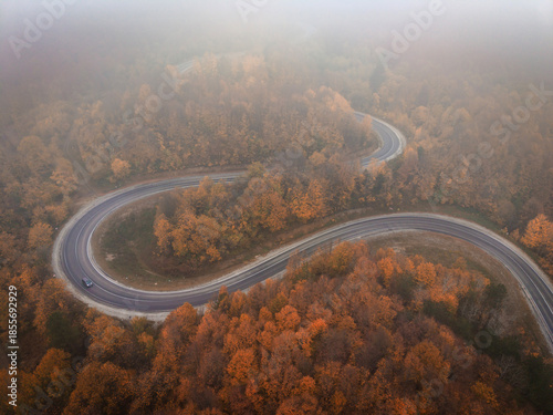 Aerial view of a single car driving on a winding foggy mountain road at sunrise