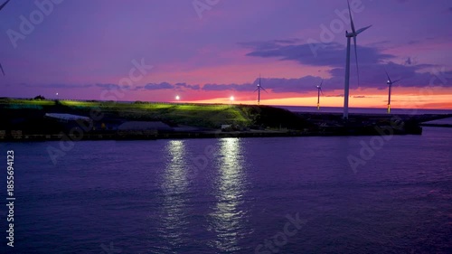 Stunning twilight scenery at Akita Port in Japan during autumn. Vibrant sunset colors illuminate the sky while wind turbines stand along the waterfront.
