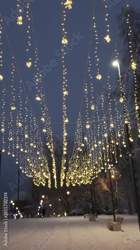 Snowy Street Canopy Of Lights Above Walkway, Warm Golden Strings Drape Over Snow Dusted Benches And Lampposts, Quiet Winter Evening, Seasonal Market Vibe With Footprints And Vendor Stalls In Soft