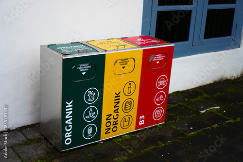 Modern recycling bins with three compartments, namely organic waste, non-organic waste, and hazardous waste (B3 waste). A set of colorful stainless steel trash cans in a public facility.