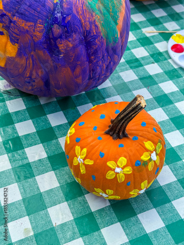 Small hand painted pumpkin decorated with yellow flower motifs placed on a green checkered tablecloth. Colourful seasonal craft concept related to autumn, harvest, halloween decoration, creativity