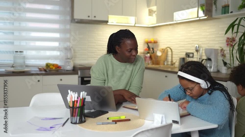 African american mother helping daughter with homework while working on laptop